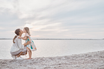 Fototapeta premium Mother, girl and kiss at beach for travel, bonding and relax with back view, sand and connection. Family, mom and child outdoor at ocean for mockup space, tropical holiday and walking in Maldives