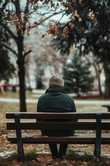 Fototapeta premium A lonely figure sitting on a bench in a quiet park during winter