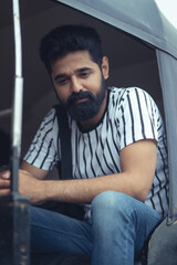 handsome indian bearded black hair man wearing casual clothes white t shirt sitting in rickshaw....