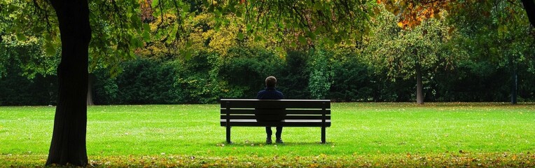 A lonely person sitting on a bench in a quiet park during autumn