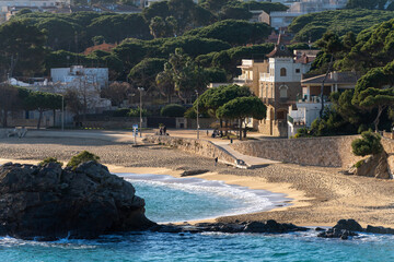 Empty beach of the Mediterranean Sea in Cala de Sant Francesc Blanes or Cala Bona during the low season in autumn, winter, or spring. Spanish coastal village with old classic houses among the cedars.