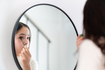 Teenage girl applying makeup, young girl putting some mascara on her eyelashes in front of a mirror