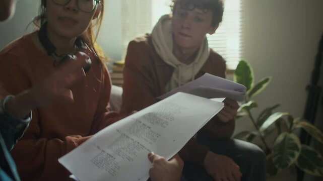 Side shot of group of diverse college students proofreading and discussing movie script before filming it, sitting in dormitory