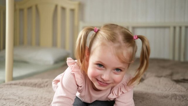 Little Girl joking sticking tongue out with silly expression. Child making face. Funny foolishness portrait of baby girl laughing in bedroom. Adorable Caucasian kid doing crazy comical gesture at home