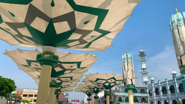 white and green color mosque with giant umbrella in the courtyard in alun alun pasuruan jawa timur has beautiful blue sky