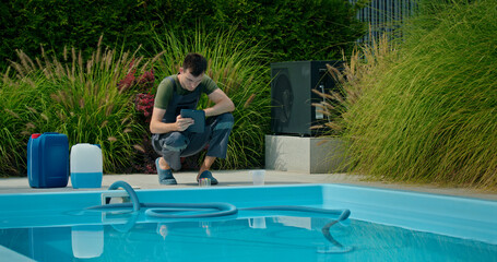 Pool maintenance technician using a tablet beside a swimming pool surrounded by ornamental grasses...