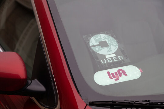 Portland, Oregon/USA-February 1, 2020: Lyft and Uber rideshare taxi company's logo emblem sign on a red rideshare vehicle parked at curbside on the street