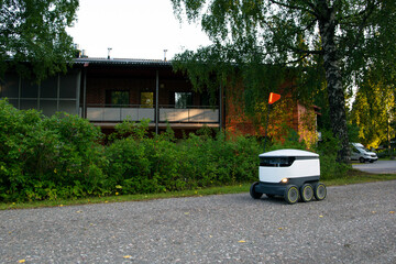 A delivery robot on wheels completes a home delivery from the grocery store. The self-driving courier navigates traffic on the road. Efficient shipping ensures quick takeaway service.