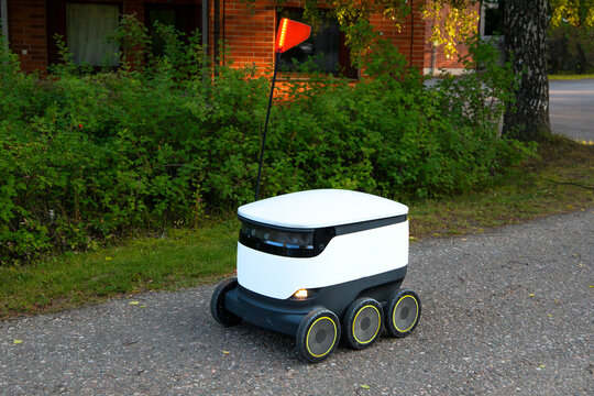 A delivery robot on wheels completes a home delivery from the grocery store. The self-driving courier navigates traffic on the road. Efficient shipping ensures quick takeaway service.