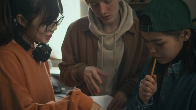 Tilt shot of team of three diverse cinematography students gathered together indoors to make edits in scenario of their movie for final project