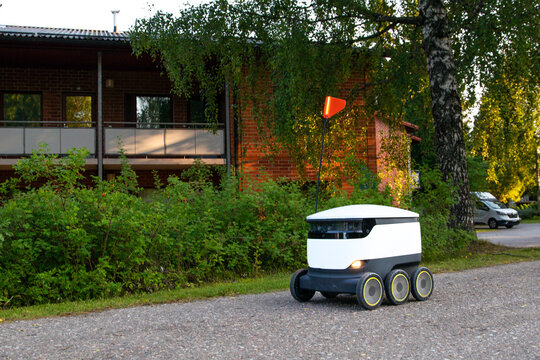 A delivery robot on wheels completes a home delivery from the grocery store. The self-driving courier navigates traffic on the road. Efficient shipping ensures quick takeaway service.