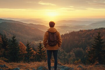 Fototapeta premium A person in a brown jacket stands on a hilltop gazing at the sunsetlit valley
