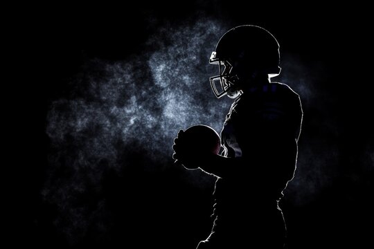Silhouette dark scene of American football player in helmet holding football.  Fog and team. Concept - Powered by Adobe