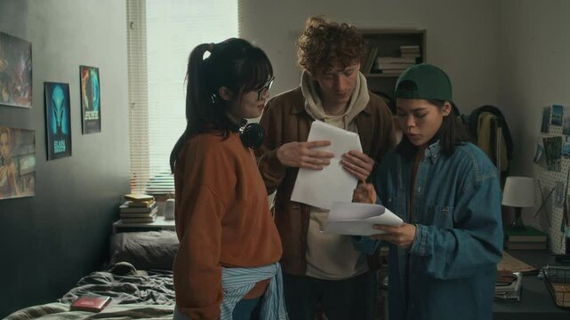 Medium shot of group of three diverse college students preparing graduate project, making amendments in film scenario at home