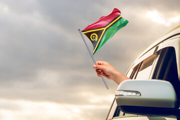 Waving the Vanuatu flag against the sunrise or sunset from a car driving along a country road. Holding the Vanuatu flag, traveling by car, on a weekend trip.