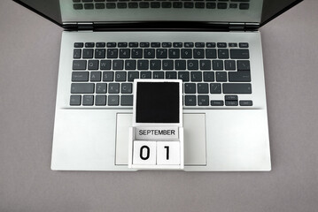 White wooden block calendar with date 01 September and laptop on gray background. Top view. Concept...