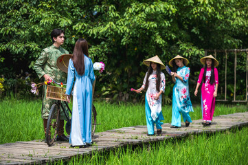 Group of young man and women in colorful AO DAI traditional Vietnam costumes walking on wood bridge in green nature park