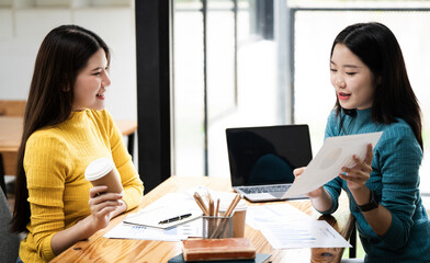 Two business women sit at desk discuss project details, diverse female colleagues meeting in office