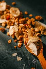 Overhead view of a wooden spoon with scattered granola, dried banana chips, and coconut flakes on a dark textured background