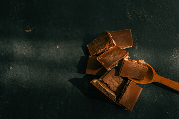Close-up view of broken chocolate pieces with layers of white and dark chocolate, placed on a wooden spoon against a dark textured background