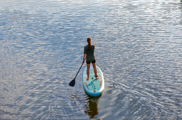 Girl paddling on SUP board on water, standing up paddle boarding adventure