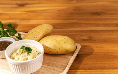 Close up mashed potato dish menu with brown gravy in wooden tray with potatoes, parsley on wooden table warm light background. Copy space text banner. Eatable international food recipe concept ideas