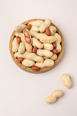 Wooden bowl with whole peanuts. Top view, on a light background.
