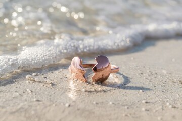 Broken heart-shaped ring on a sandy beach with gentle waves in the background.
