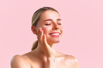 Portrait of a beautiful young woman applying eye cream and smiling with closed eyes. Skin care concept.