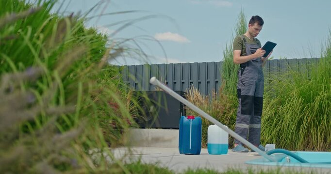 A technician performs routine pool maintenance using a tablet, with chemical containers and a pool vacuum close by.