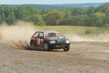 A close-up of an autocross racing car. Clouds of dust and sand burst out from under the wheels....