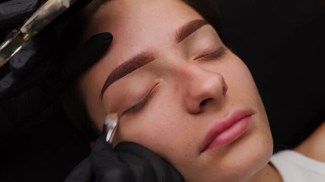 Applying facial tinting cream to a girl's eyelid. Light permanent eyebrow makeup, performing eyebrow tattooing
