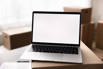 Close up laptop with white mock up on screen, placed on top of big cardboard box. Transportation services for relocation day, logistics, inventory management, electronic commerce marketplace platform
