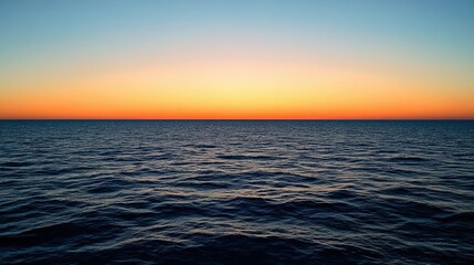 Obraz premium A panoramic view of the open sea at twilight, with the sky transitioning from orange to deep blue and the water calm.