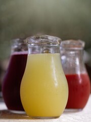 Three decanters of different kind of juice on a table with a blurred green background. Variety of...