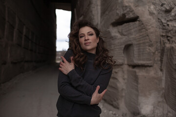 A beautiful woman dressed in gray pants and a sweater walks against the background of a career in stylish clothes