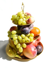 Decadent gold tiered fruit platter isolated on white background, apple, banana, grapes, mandarine orange, fig, mango, plum, detailed, close up.