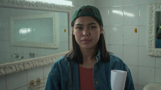 Chest up portrait of young Caucasian female operator in casual clothes and cap making hand frame in movie set and looking at camera