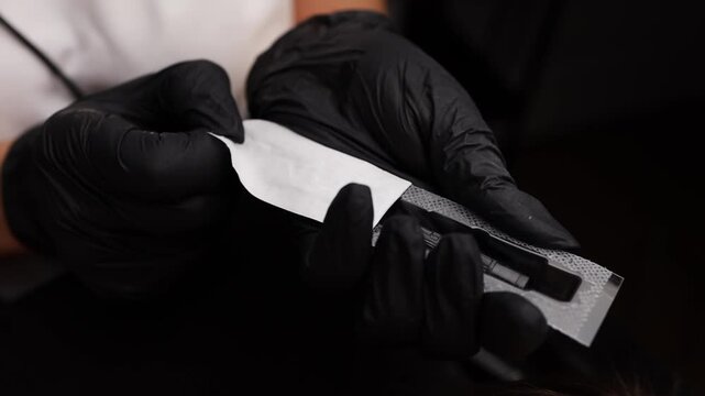 Master's hands in black gloves open a sterile tattoo cartridge. Light permanent eyebrow makeup, performing eyebrow tattooing