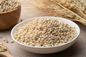 Uncooked barley grain seeds, pearl barley in white plate on wood table
