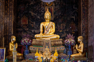 Obraz premium Thailand, August 11, 2024, Wat Phitchaya Yatikaram Worawihan, Golden Buddha statue surrounded by smaller figures and floral arrangements in a serene temple setting