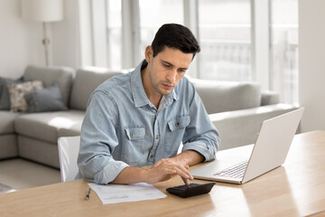 Serious young Latin homeowner man calculating domestic expenses, loan, mortgage fees, checking...