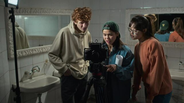 Full medium shot of team of diverse students from film college watching movie takes in restroom and high fiving, being happy for good teamwork, recording movie for graduate project