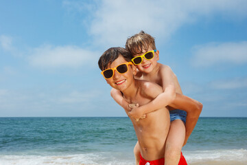 Two boys wear sunglasses enjoy piggyback ride on sunny beach day