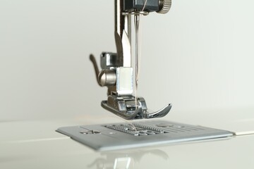Sewing machine with beige thread on light background, closeup