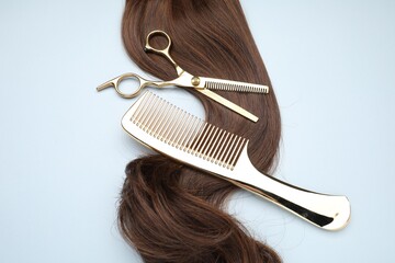 Brown hair strand, comb and professional scissors on light grey background, top view