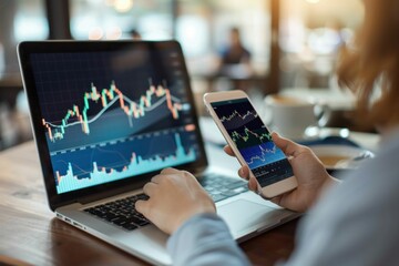 Person analyzing financial data on a laptop and smartphone in a cafe setting