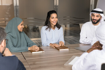 Cheerful multiethnic Arabian and European coworkers having fun, talking at meeting table, brainstorming on creative project, attending training, laughing, enjoying offline diverse communication