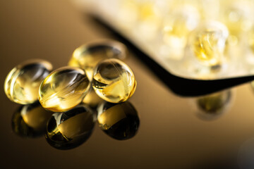 Golden Yellow Transparent Capsules of Vitamin D and Fish Oil Omega 3 on Reflective Surface for Dietary Supplement Use