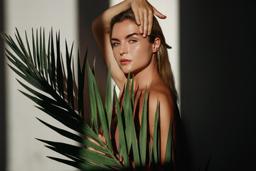 Young woman with blonde hair is holding a palm leaf  in sunlight